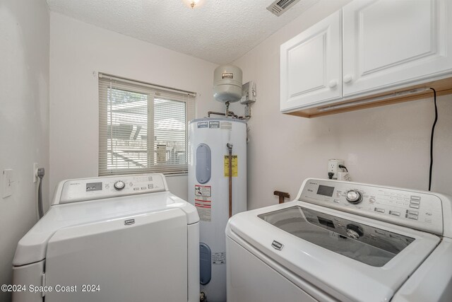 laundry area with cabinets, electric water heater, a textured ceiling, and washing machine and dryer