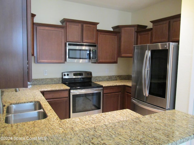 kitchen featuring kitchen peninsula, light stone counters, sink, and stainless steel appliances