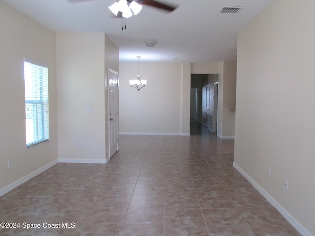 tiled spare room with ceiling fan with notable chandelier