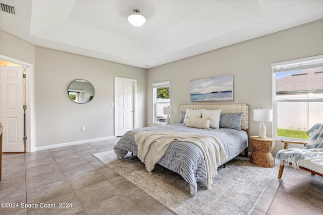 tiled bedroom featuring a raised ceiling and multiple windows