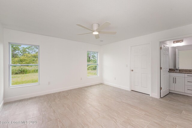 unfurnished bedroom featuring multiple windows, ensuite bath, ceiling fan, and sink