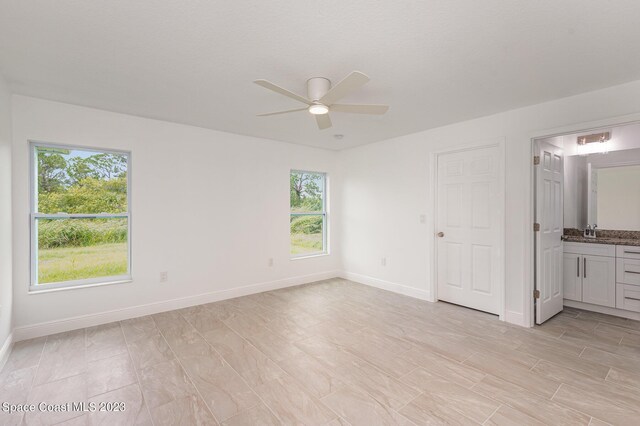 unfurnished bedroom with baseboards, ensuite bath, ceiling fan, and a sink