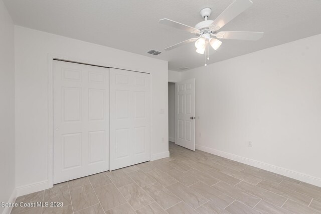 unfurnished bedroom with a closet, a textured ceiling, visible vents, baseboards, and a ceiling fan