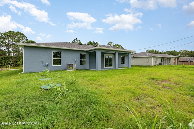 back of property with stucco siding, central AC, and a yard