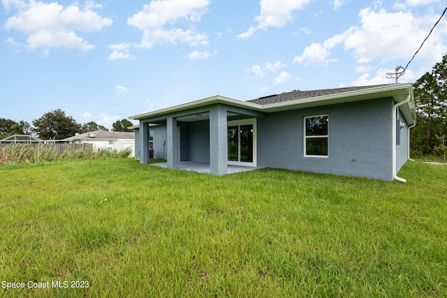 rear view of house featuring a lawn, stucco siding, and a patio