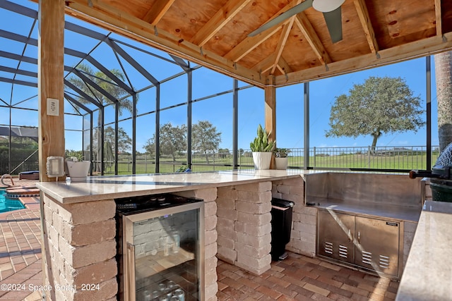 view of patio with a lanai, wine cooler, a bar, area for grilling, and ceiling fan