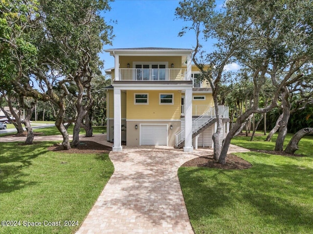 coastal home featuring a balcony, a garage, and a front lawn