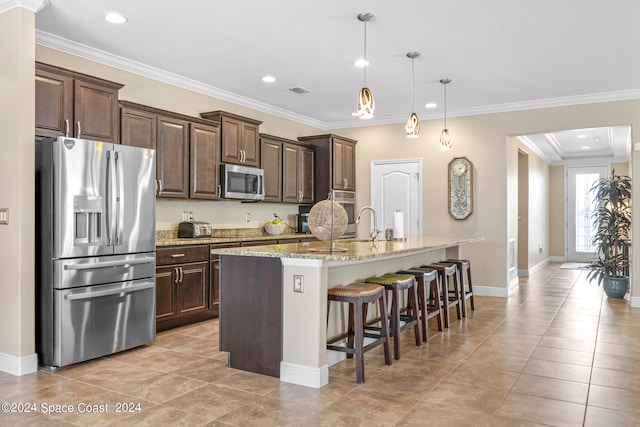 kitchen with an island with sink, stainless steel appliances, ornamental molding, and a breakfast bar area