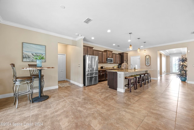 kitchen featuring an island with sink, hanging light fixtures, ornamental molding, appliances with stainless steel finishes, and a kitchen breakfast bar