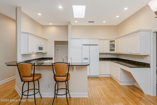 kitchen featuring a skylight, white appliances, light hardwood / wood-style flooring, white cabinetry, and dark stone counters