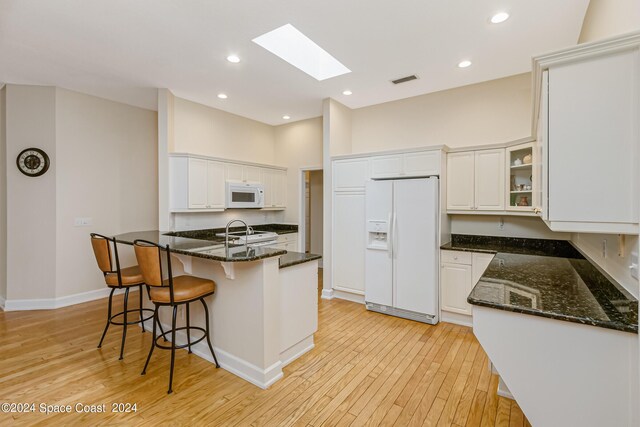 kitchen featuring white cabinets, white appliances, light wood-type flooring, a skylight, and dark stone counters