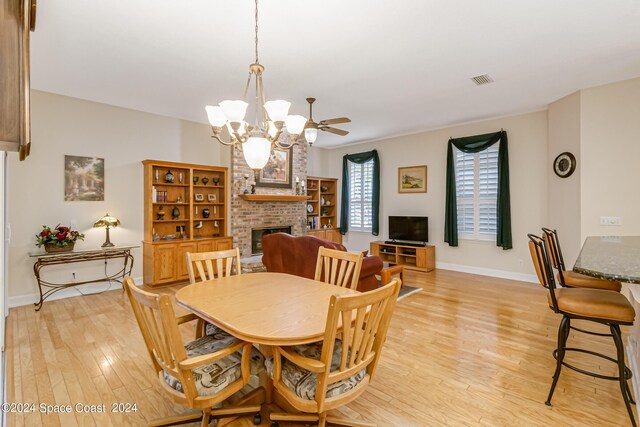 dining space with ceiling fan with notable chandelier, light hardwood / wood-style floors, and a fireplace