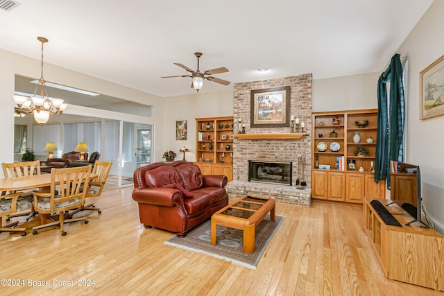 living room featuring ceiling fan with notable chandelier, light hardwood / wood-style floors, and a brick fireplace