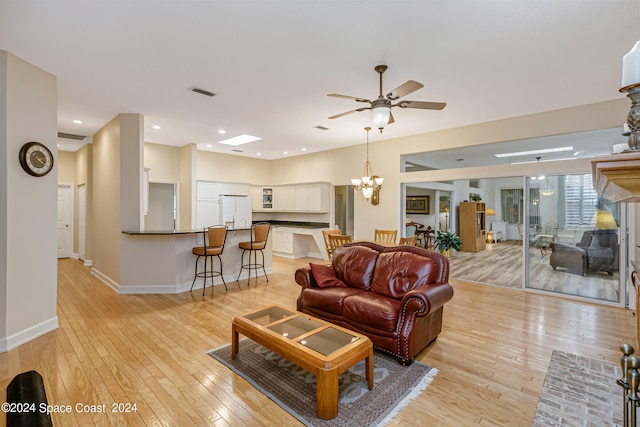 living room with ceiling fan with notable chandelier and light hardwood / wood-style floors