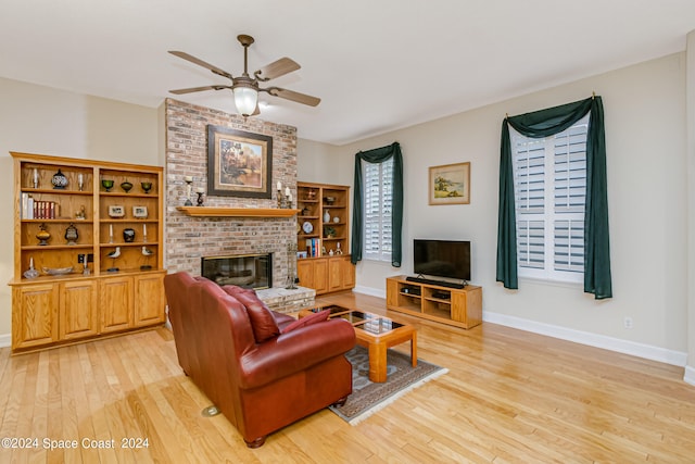 living room featuring a brick fireplace, light wood-type flooring, and ceiling fan