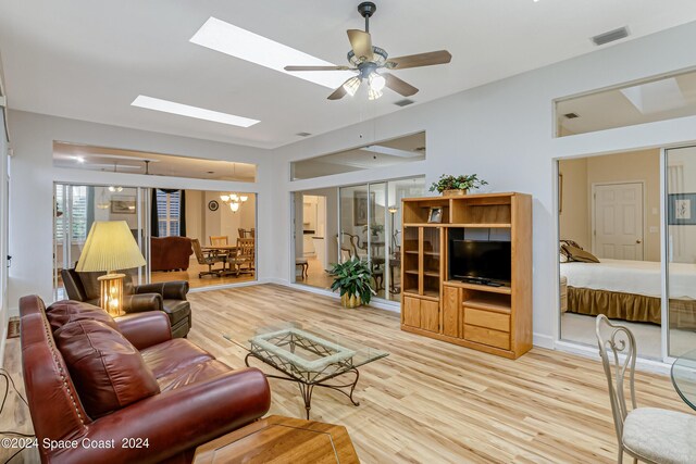 living room featuring ceiling fan, a skylight, and light wood-type flooring