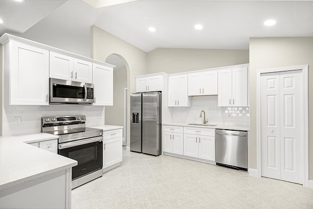 kitchen with sink, lofted ceiling, white cabinetry, decorative backsplash, and appliances with stainless steel finishes