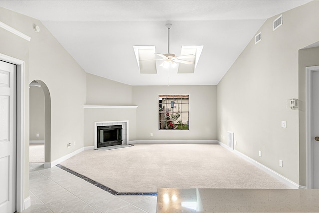 unfurnished living room with vaulted ceiling with skylight, a tiled fireplace, light carpet, and ceiling fan