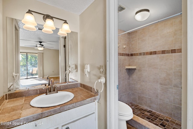 bathroom with vanity, ceiling fan, toilet, a textured ceiling, and tiled shower