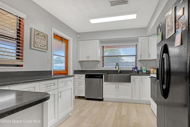 kitchen with white cabinetry, sink, light hardwood / wood-style flooring, stainless steel dishwasher, and black refrigerator