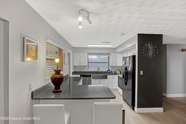 kitchen featuring dishwasher, sink, black fridge, white cabinets, and light wood-type flooring