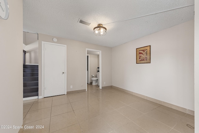 unfurnished bedroom with a textured ceiling, light tile patterned flooring, and ensuite bathroom