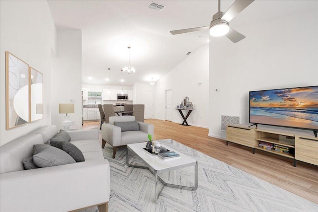 living room with ceiling fan with notable chandelier, vaulted ceiling, and light hardwood / wood-style floors