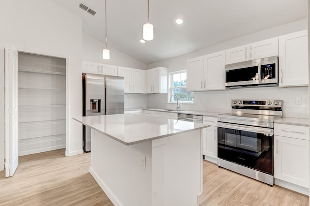 kitchen with white cabinets, vaulted ceiling, appliances with stainless steel finishes, and a kitchen island