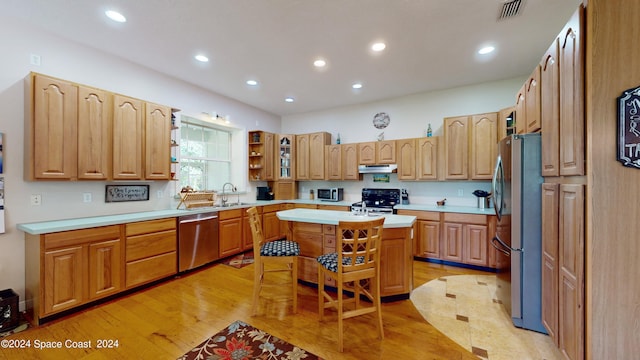 kitchen with sink, a breakfast bar area, a center island, stainless steel appliances, and light wood-type flooring