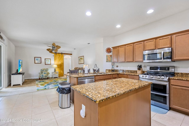 kitchen featuring light stone counters, kitchen peninsula, a kitchen island, a barn door, and appliances with stainless steel finishes