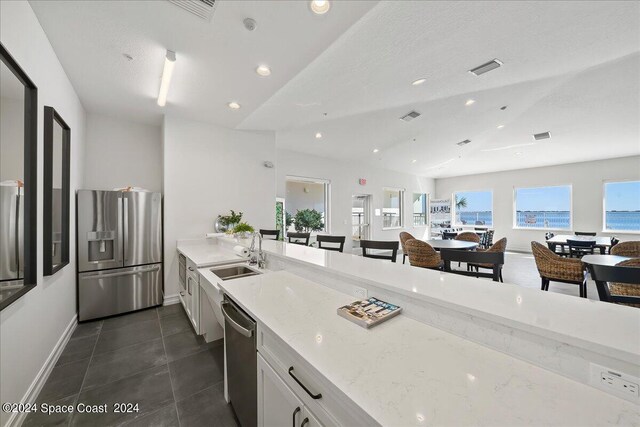 kitchen with light stone counters, lofted ceiling, sink, white cabinetry, and stainless steel appliances