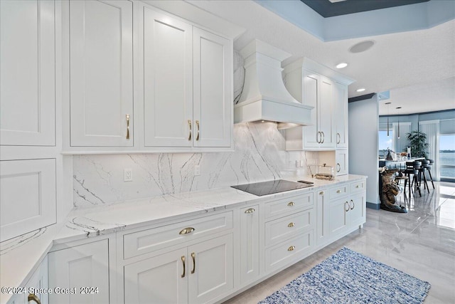 kitchen featuring black electric stovetop, light stone counters, white cabinets, decorative backsplash, and premium range hood