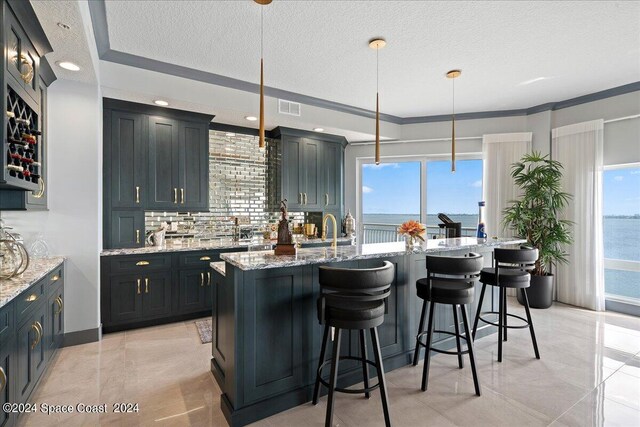 kitchen featuring hanging light fixtures, a water view, an island with sink, and plenty of natural light