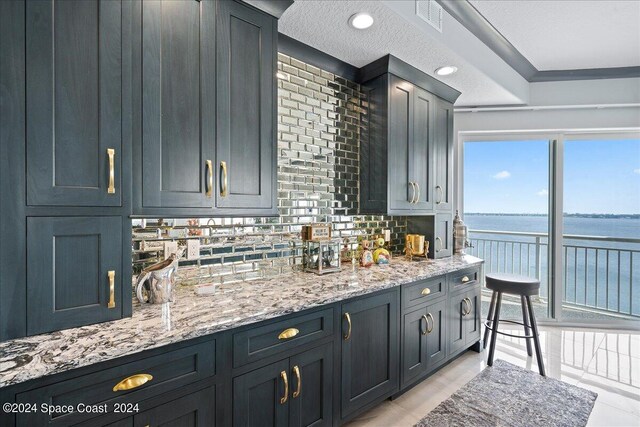 kitchen with light stone countertops, a water view, a textured ceiling, and tasteful backsplash