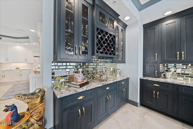 bar with light stone countertops, backsplash, a textured ceiling, and light tile patterned flooring