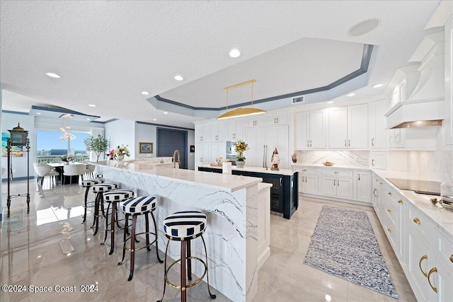 kitchen with white cabinets, hanging light fixtures, a large island with sink, backsplash, and a breakfast bar