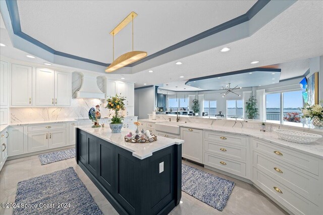 kitchen with white cabinetry, hanging light fixtures, decorative backsplash, a raised ceiling, and premium range hood