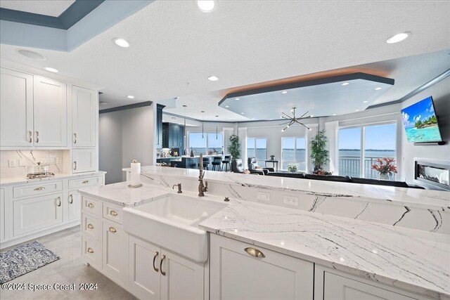 kitchen featuring light stone counters, white cabinets, a textured ceiling, and sink