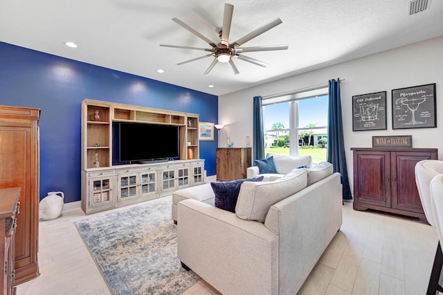 living room with a textured ceiling, ceiling fan, and light hardwood / wood-style flooring