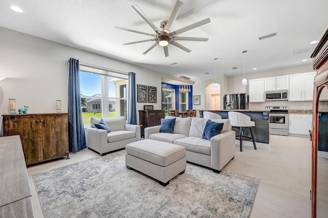 living room with ceiling fan, a textured ceiling, and light wood-type flooring