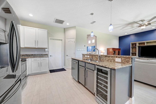 kitchen featuring appliances with stainless steel finishes, decorative light fixtures, sink, white cabinets, and beverage cooler