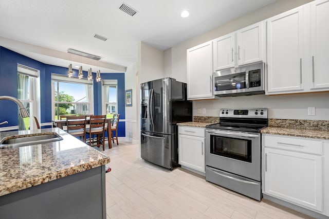 kitchen featuring stainless steel appliances, light stone counters, white cabinets, sink, and pendant lighting