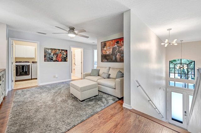 living room featuring separate washer and dryer, ceiling fan with notable chandelier, and light hardwood / wood-style flooring