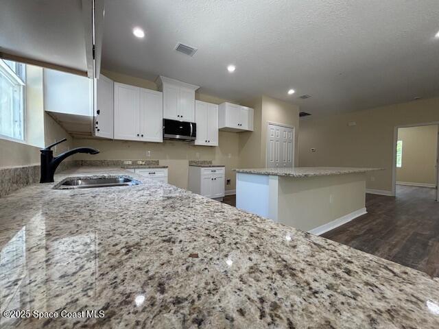 3250 San Jose Ave SE, Palm Bay, FL 32909 - kitchen with a sink, stainless steel microwave, light stone counters, white cabinetry, and a center island