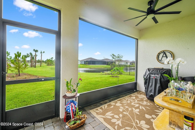 sunroom / solarium featuring a water view, plenty of natural light, and a ceiling fan