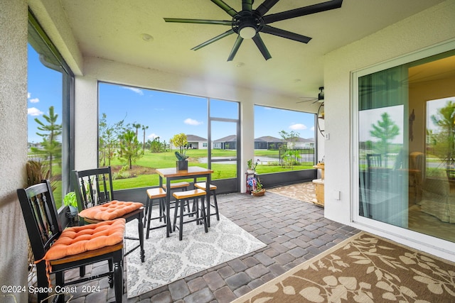 sunroom with ceiling fan, a residential view, and brick floor
