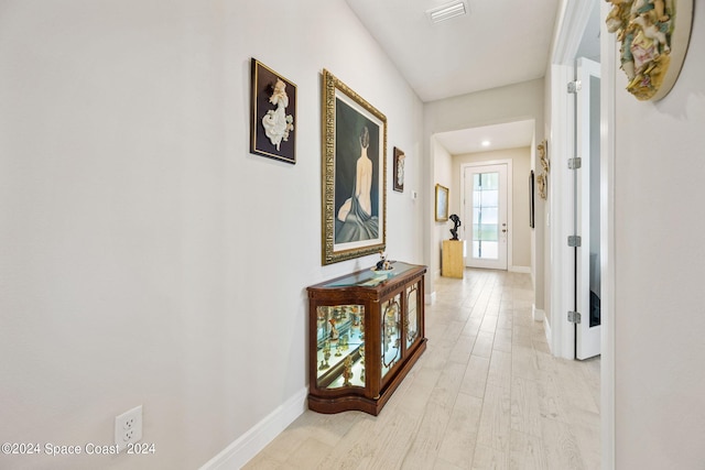 corridor with baseboards, light wood finished floors, and visible vents