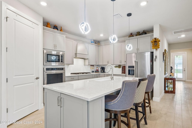 kitchen featuring hanging light fixtures, stainless steel appliances, custom exhaust hood, light hardwood / wood-style flooring, and sink