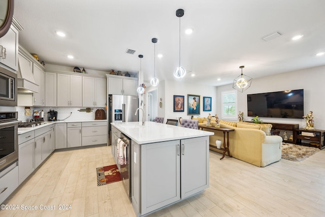 kitchen with light wood-type flooring, gray cabinetry, pendant lighting, and an island with sink