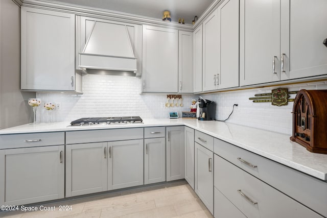 kitchen featuring premium range hood, gray cabinetry, stainless steel gas cooktop, and tasteful backsplash